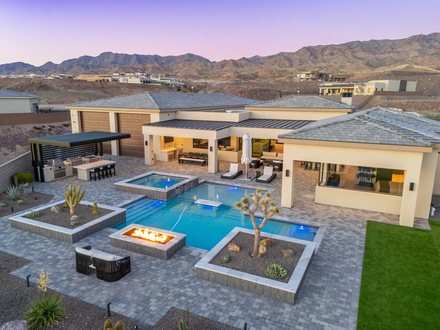Aerial view of a Janecek custom home at dusk with pool, spa, fire feature, and outdoor kitchen against the Lake Havasu mountains