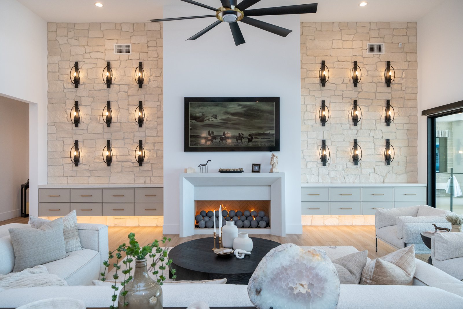 A Janecek custom home great room, stone walls, iron sconces, and a sculptural fireplace