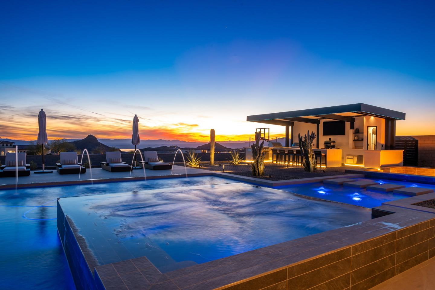 A Janecek custom home at dusk, glowing pool, lit ramada, and sunset over the desert