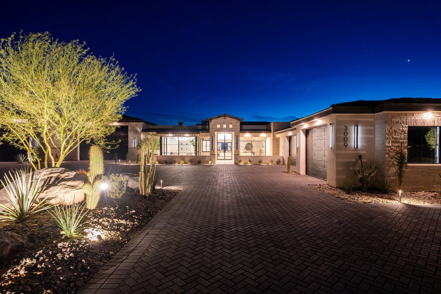 A Janecek custom home at twilight, lit entry and paver driveway
