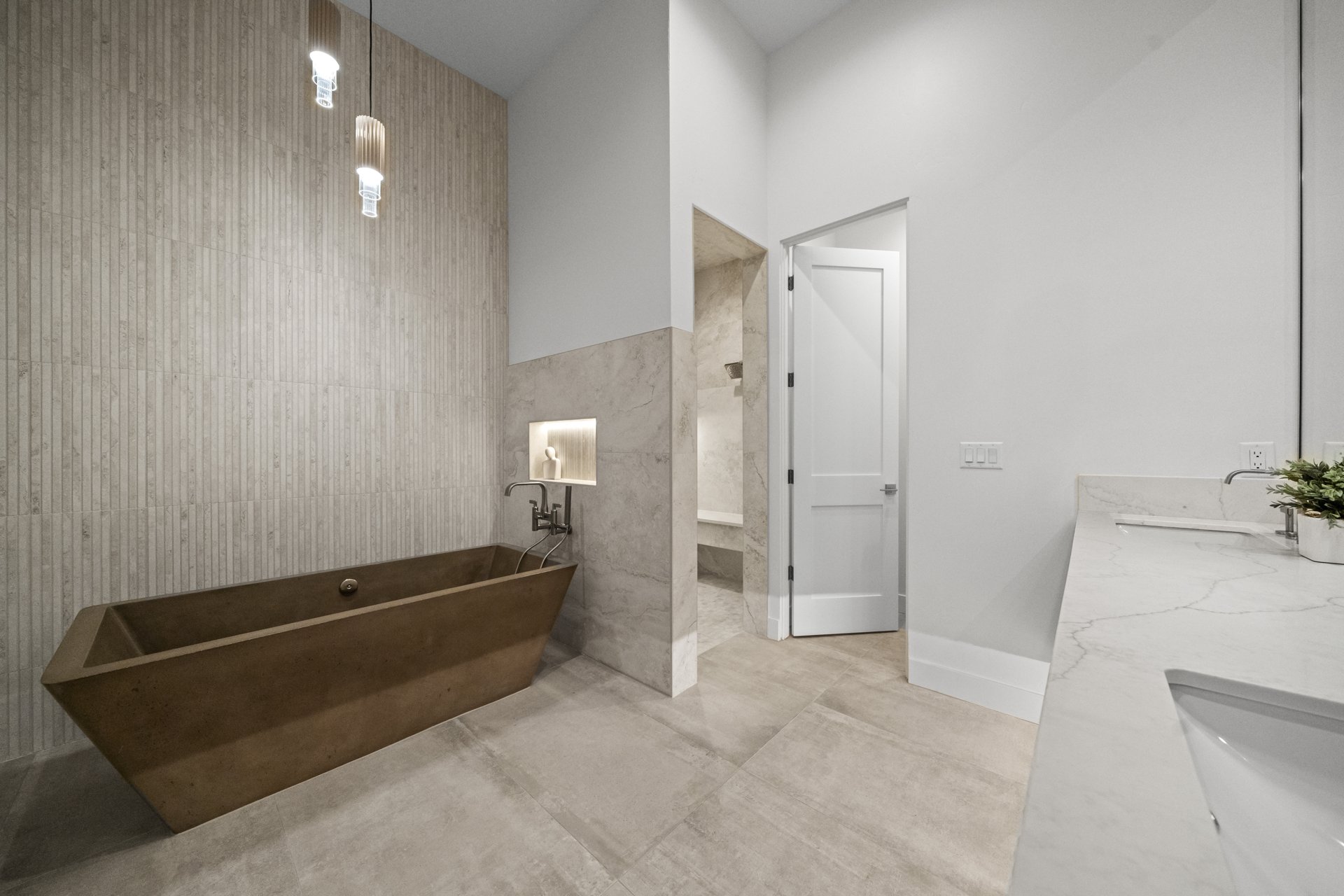 Bronze concrete soaking tub beneath pendant lights with a fluted tile accent wall