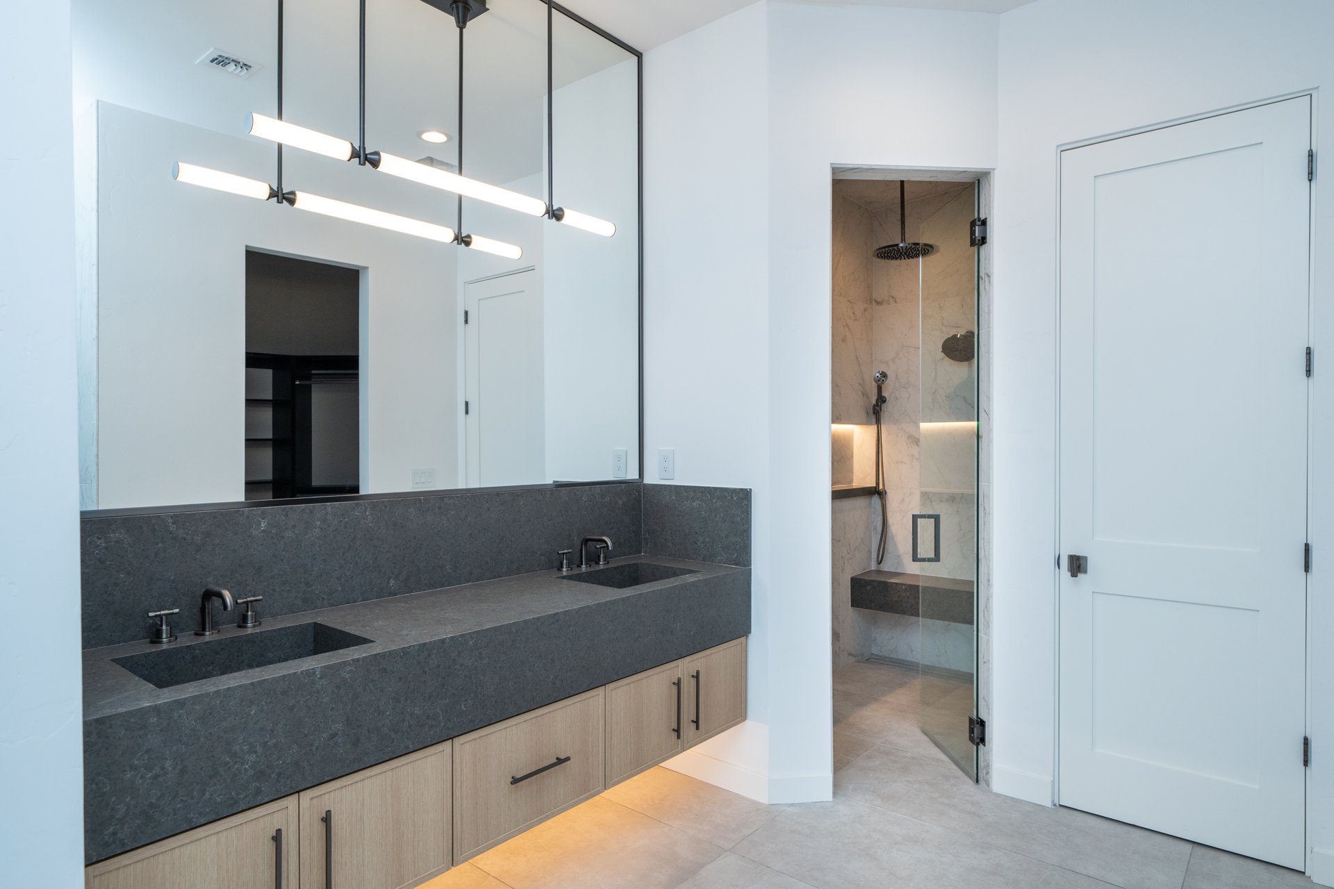 Charcoal quartz double vanity with white oak cabinetry and glass steam shower beyond