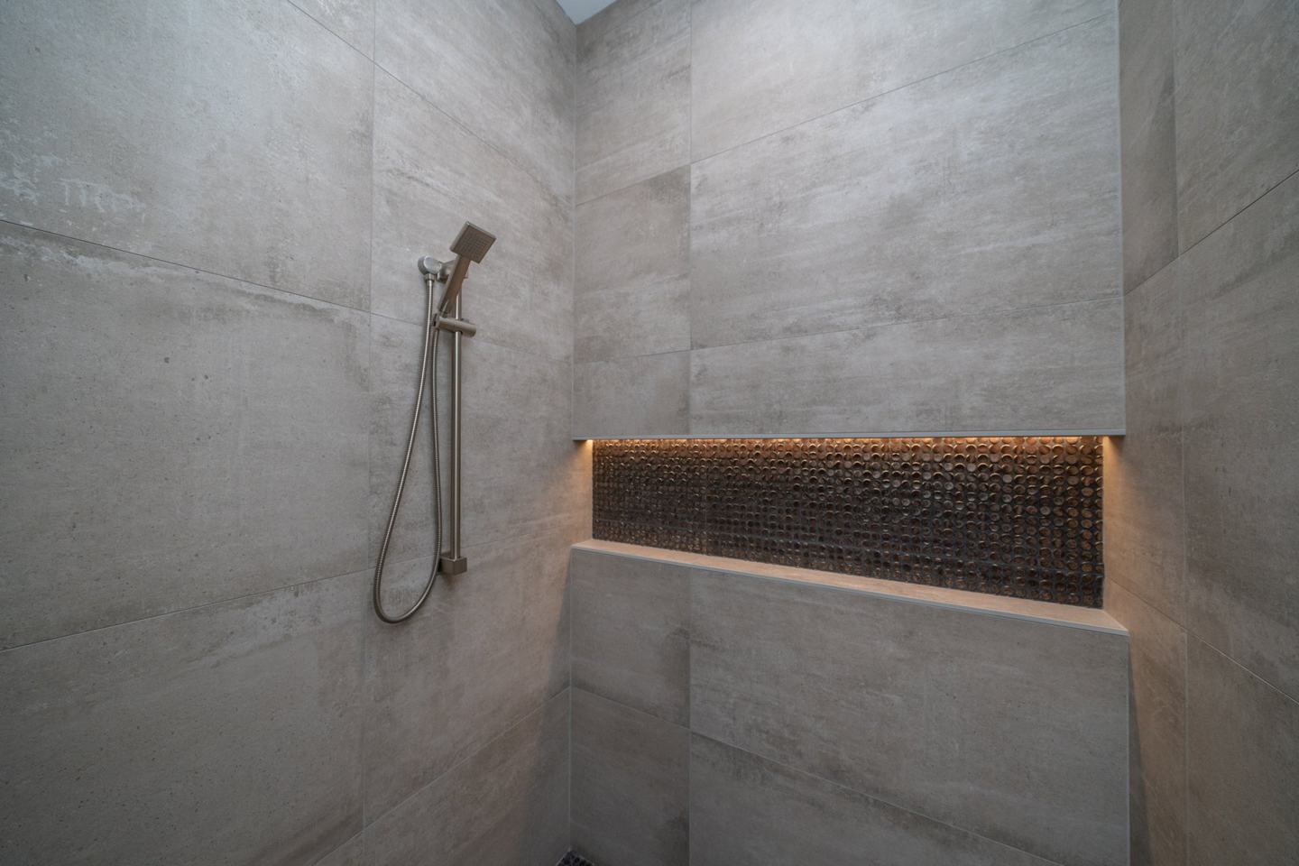 Concrete-look shower with a lit copper penny-tile niche