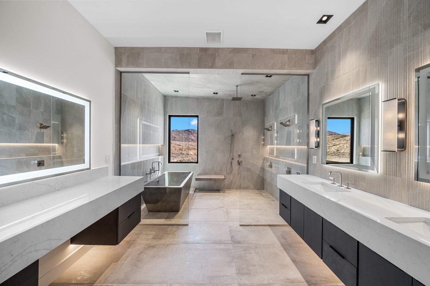 Primary bath with facing floating vanities, steel soaking tub, and glass shower wall