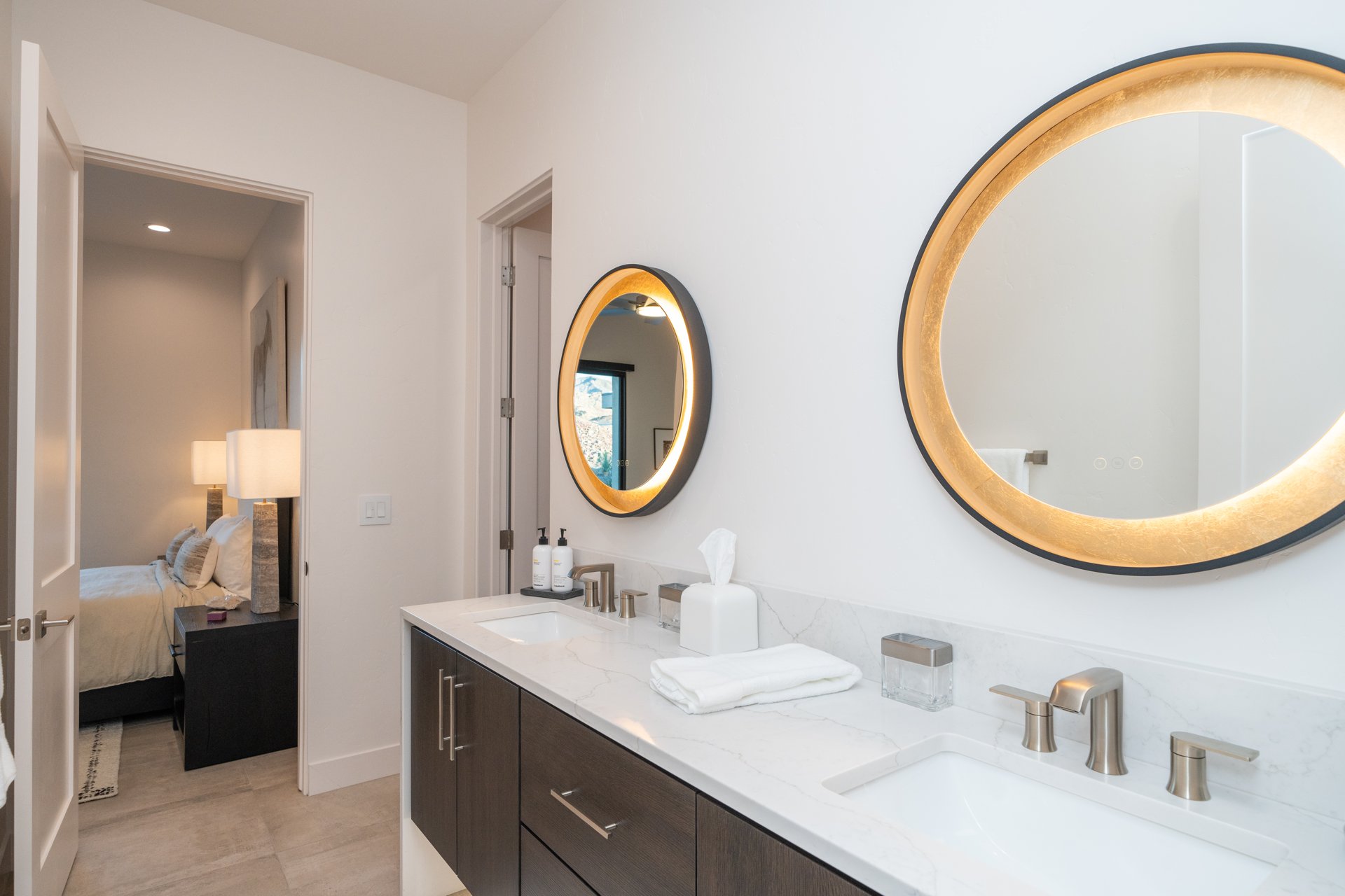 Guest bath with backlit round mirrors, double sinks, and dark wood floating vanity