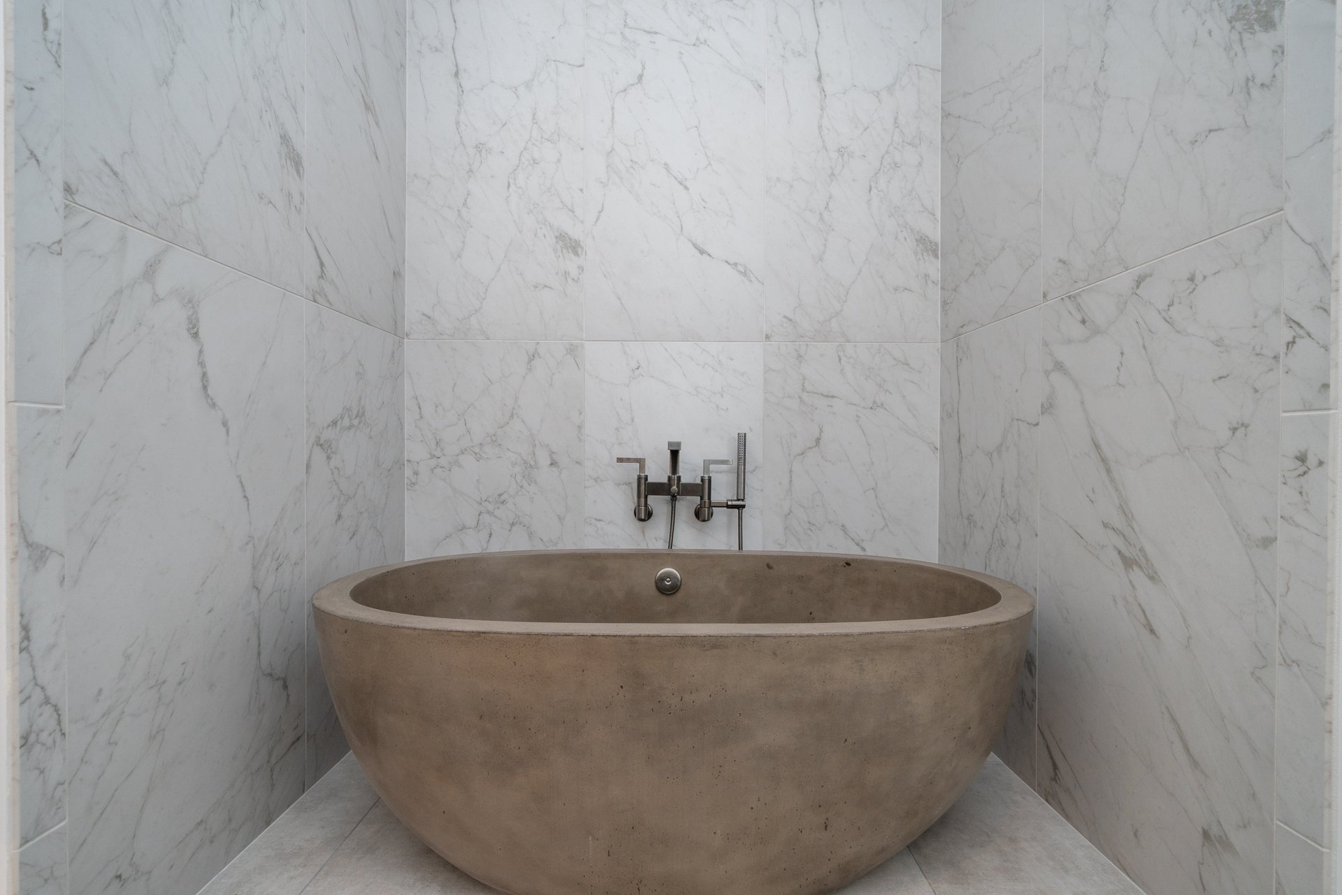 Round concrete soaking tub in a marble tiled alcove with wall mounted filler
