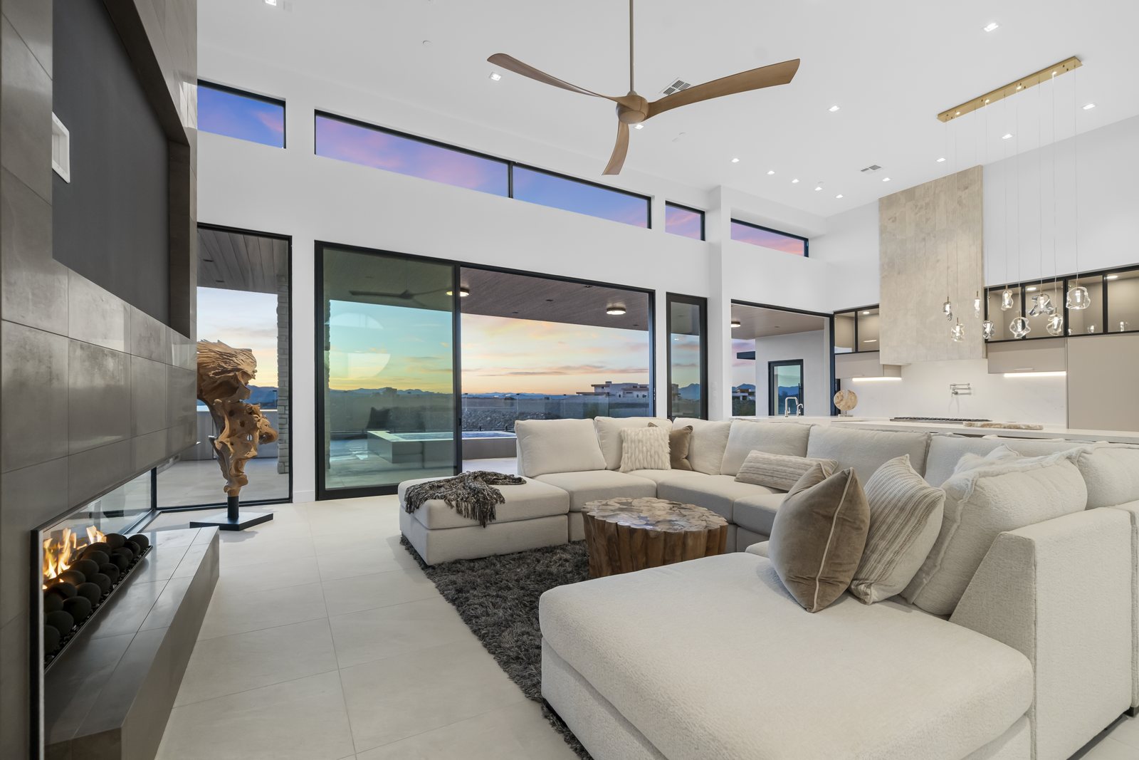 Great room with a linear fireplace, vaulted ceiling, and sliding glass wall opening to a sunset desert view