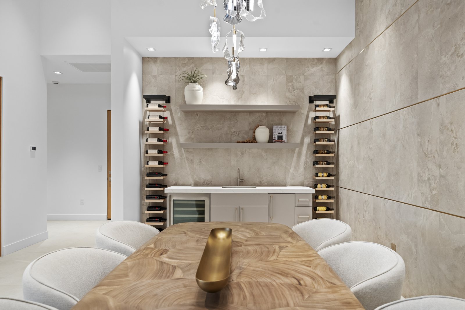 Wine and tasting room with vertical bottle displays flanking a wet bar, floating stone shelves, and a sculptural chandelier
