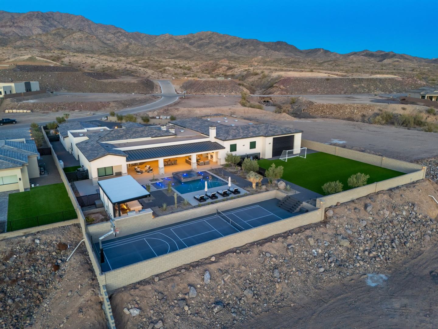 Aerial view of a custom Janecek estate with pool, sport court, and lawn against the mountains