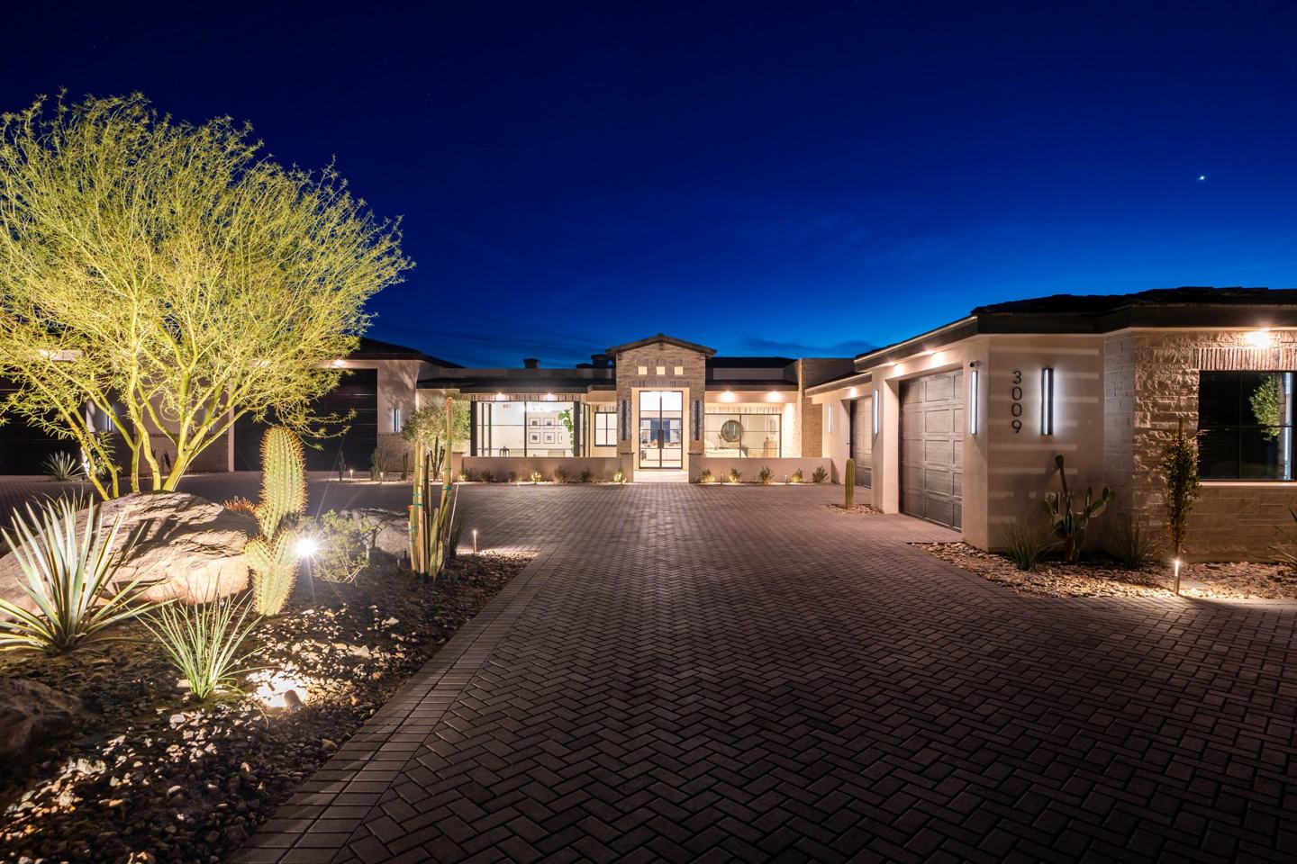 Herringbone paver driveway with uplit palo verde and cactus landscaping at twilight