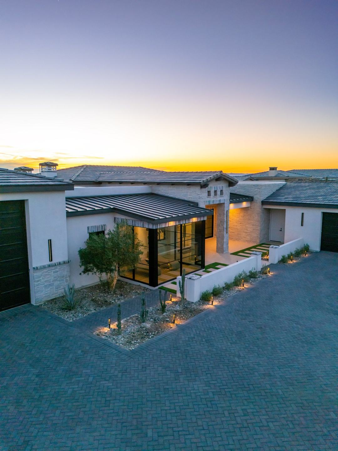 Elevated view of a custom home at sunset with a glass corner room and tile roofs