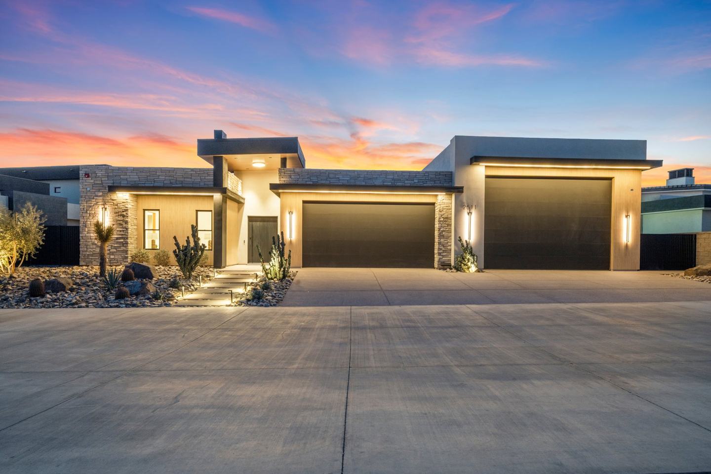 Front elevation of a custom home at sunset with stacked stone and a glass garage