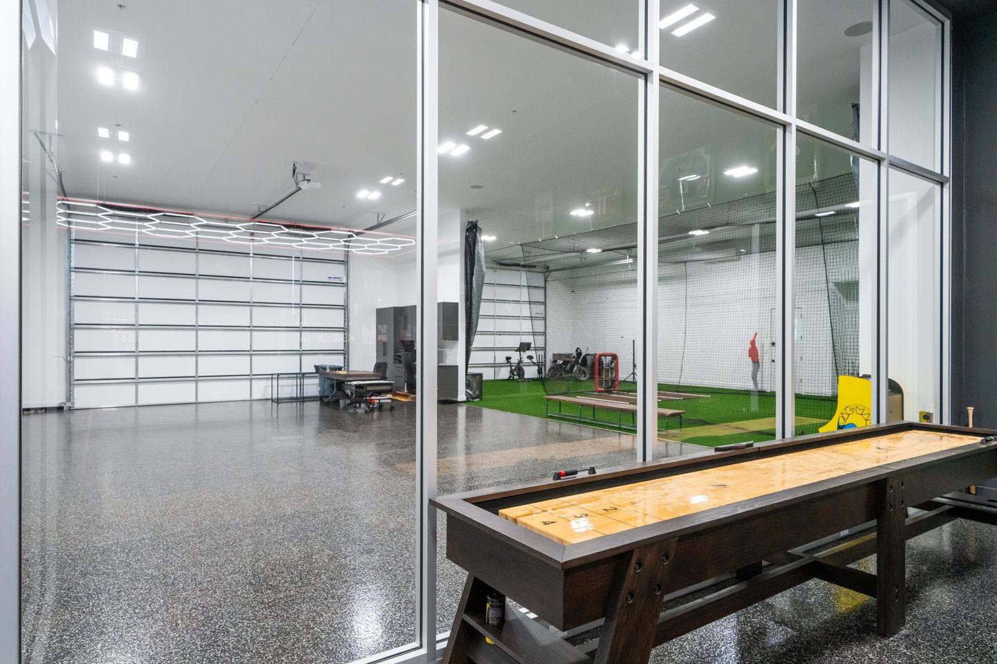 Shuffleboard table beside a glass wall overlooking the garage and indoor batting cage