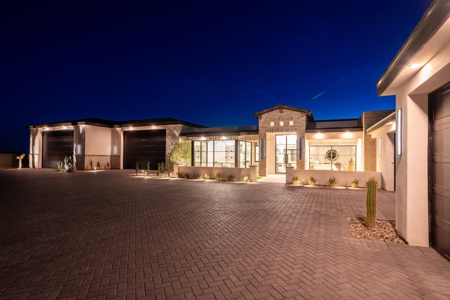 Paver motor court and illuminated front elevation of a custom desert home at twilight