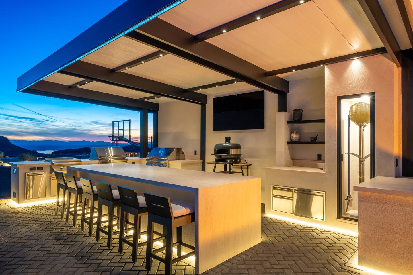 Covered outdoor kitchen and bar with lake views at twilight