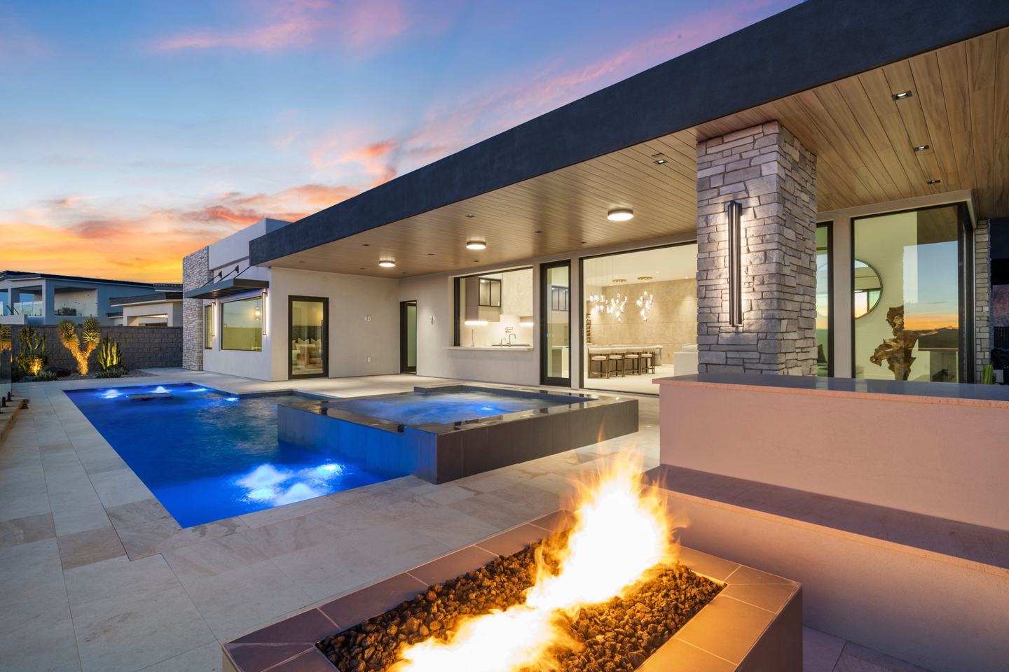 Backyard pool, spa, and linear fire feature beneath a covered patio at sunset