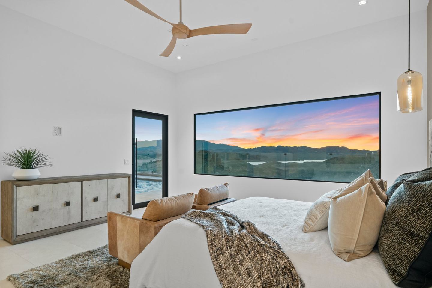Primary bedroom with a panoramic picture window framing a desert sunset over the lake