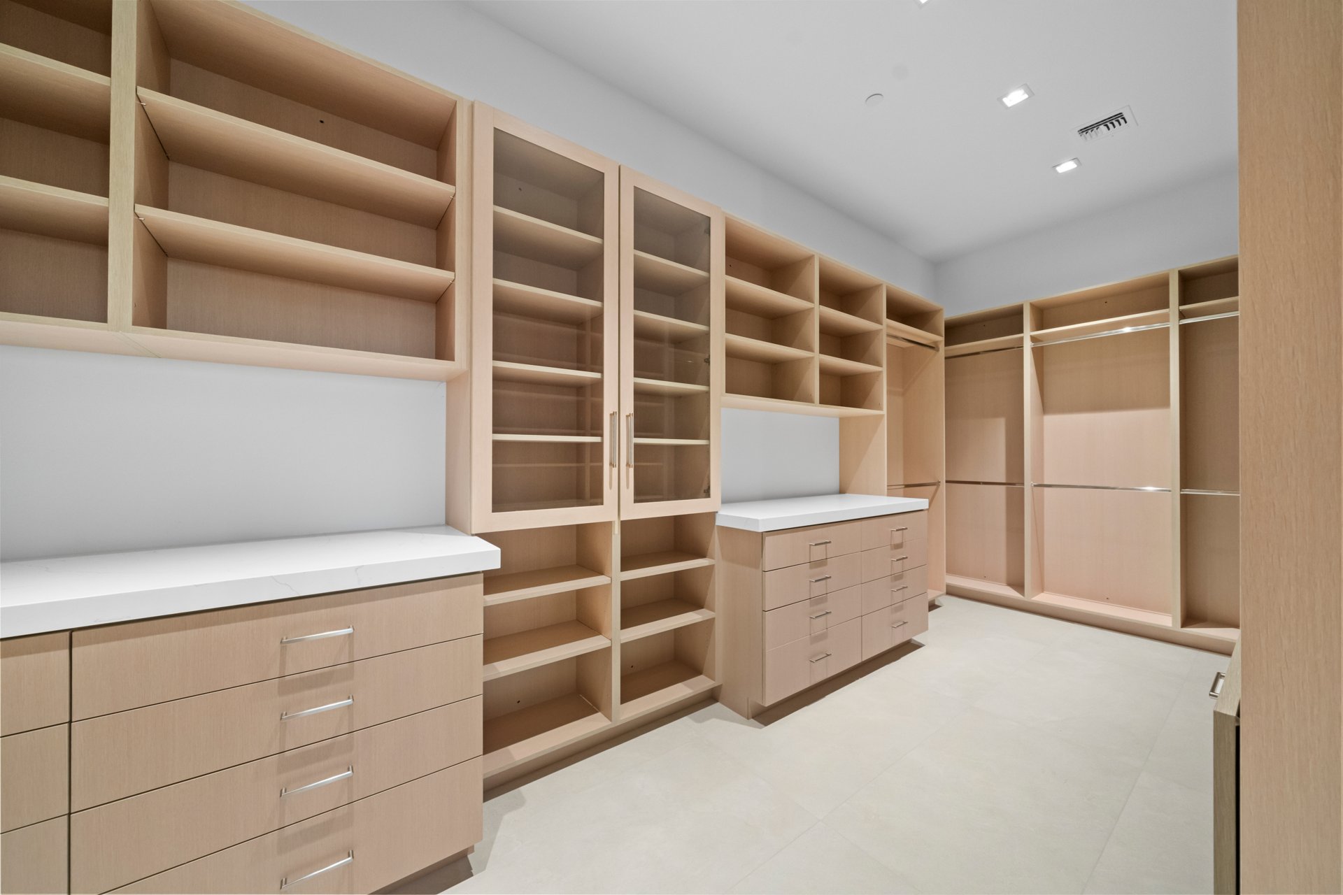 Custom walk-in closet with white oak cabinetry, glass display doors, and quartz counters
