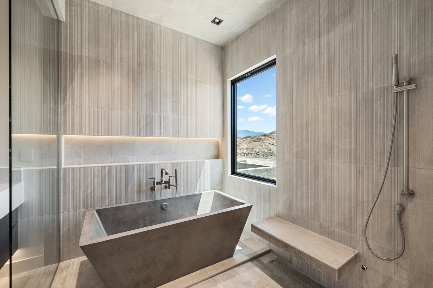 Concrete freestanding soaking tub beneath a picture window with desert mountain views