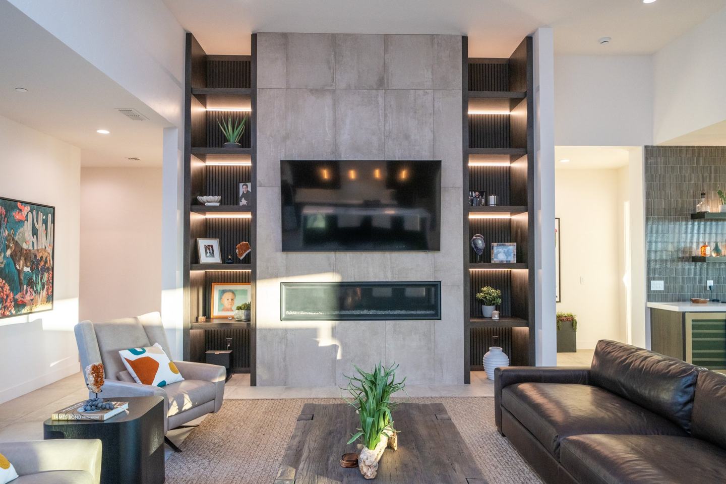 A Janecek great room with a floor-to-ceiling stone fireplace wall, a flush linear fire, and hand-built reeded display towers lit from within