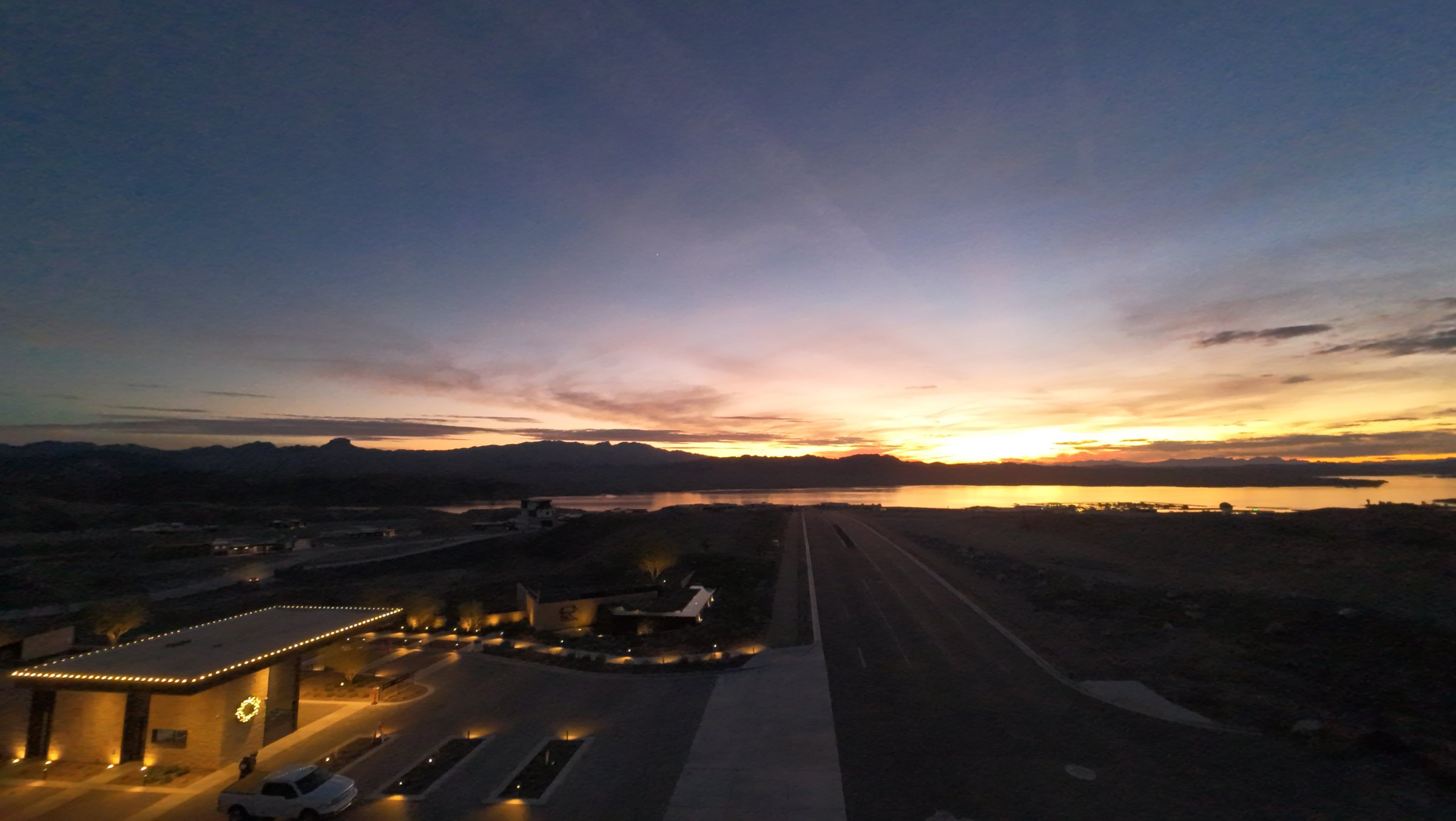 Aerial view of the Riviera Lake Havasu entrance at sunset, the lake glowing on the horizon beyond the desert hills
