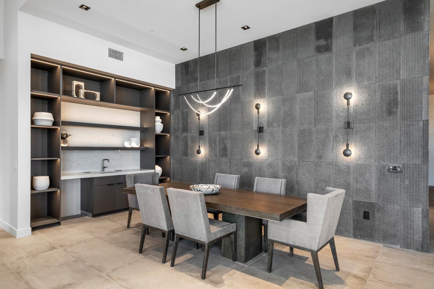 Formal dining room with a textured stone wall, sculptural lighting, and a lit built-in bar