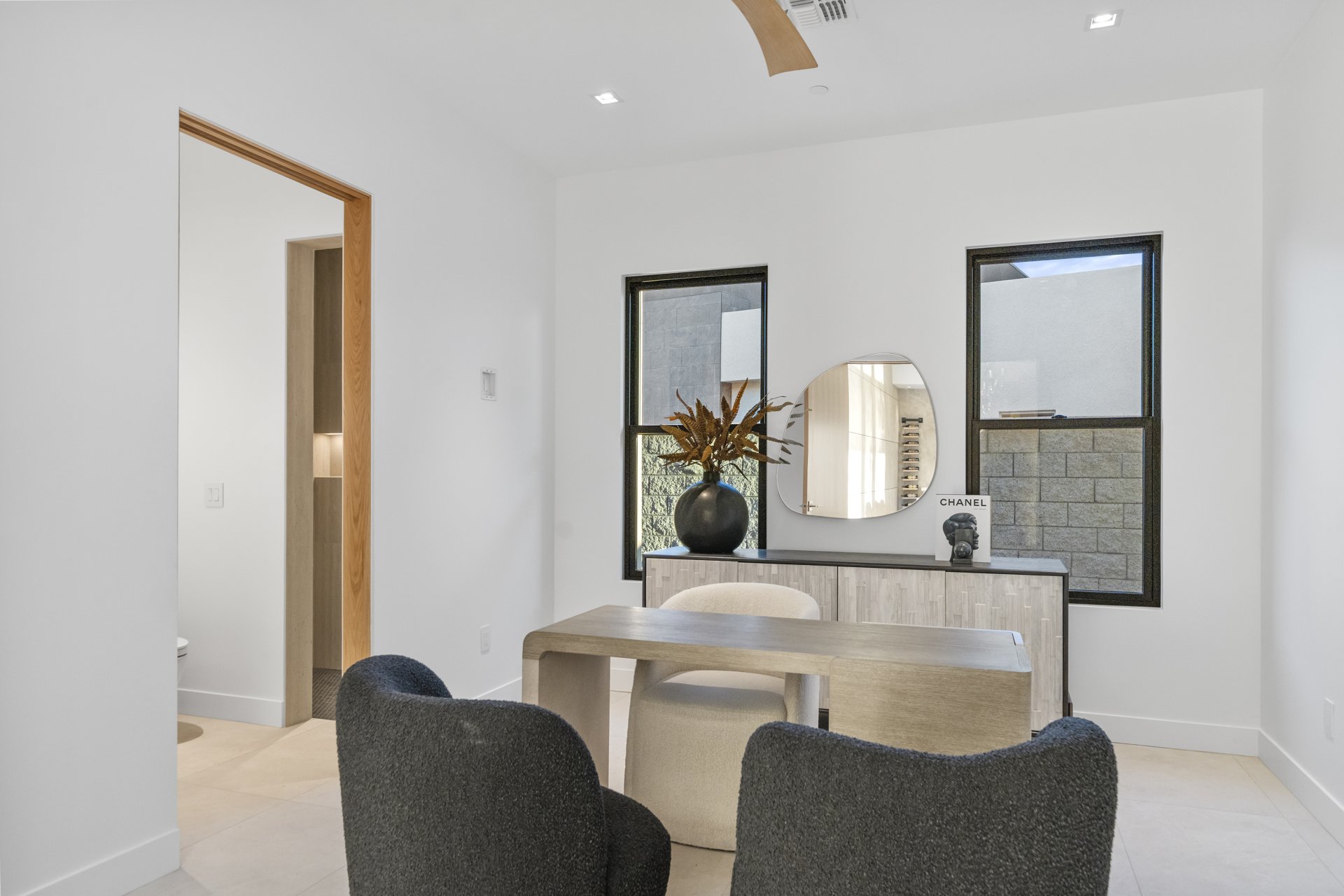 Study nook with a wood desk, boucle chairs, and a sculptural mirror between windows