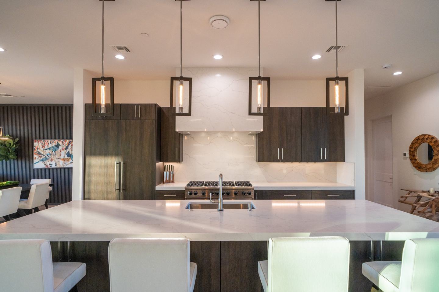 Kitchen with dark cabinetry, marble backsplash, and a large island with pendant lighting