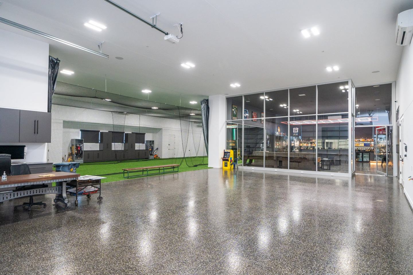 Indoor training hall with batting cage, office area, and glass walled bar lounge