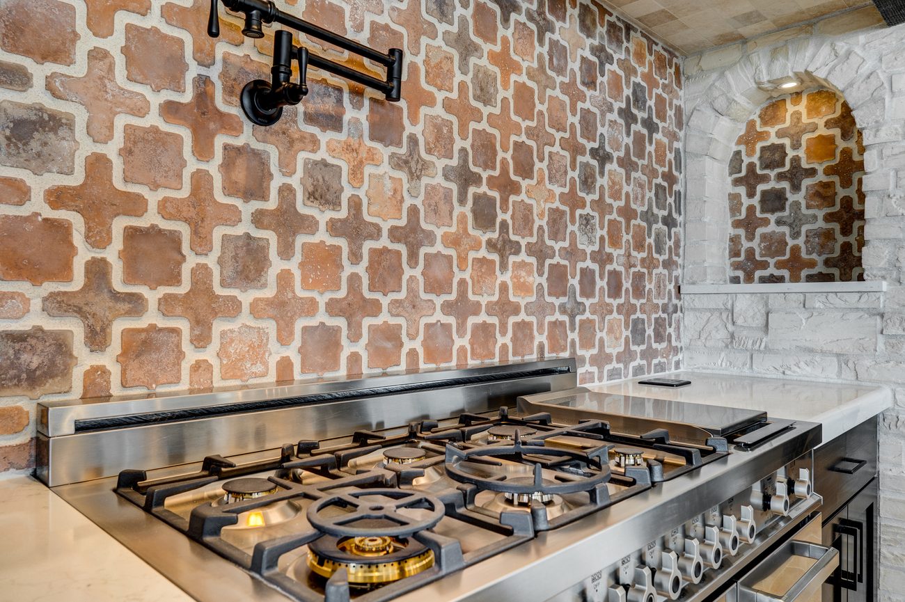 Professional gas range with a brass pot filler and terracotta arabesque tile backsplash